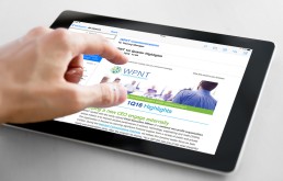 A hand is touching a tablet displaying an email from WPNT Communications with 