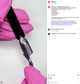 Close-up of a hand in pink gloves holding a metallic nail polish swatch. The polish has a shimmery, magnetic effect, set against a white background.